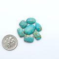 Kings Manassa Turquoise cabochons, polished green-blue gemstones with natural matrix on a white background with a US dime for scale